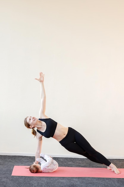 Una joven madre con un niño hace yoga en una colchoneta deportiva