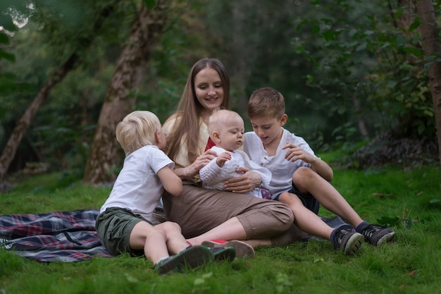 Joven madre con niños pequeños haciendo picnic en verano. Familia feliz sentado en el prado