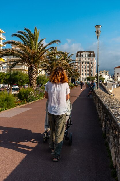 Una joven madre paseando a su hijo en el coche en verano en la Grande Plage en Saint Jean de Luz, vacaciones en el sur de Francia, País Vasco francés