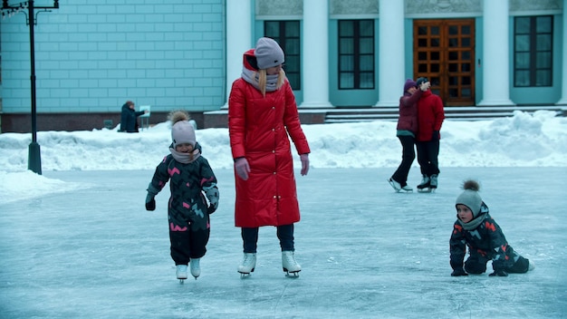 Una joven madre patinando sobre hielo con sus hijos ayudándolos a levantarse del hielo