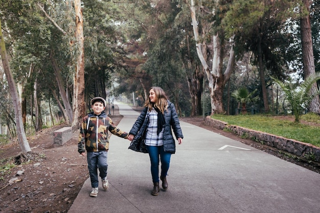 Foto joven madre rubia caminando y hablando con su hijo pequeño en una calle del parque familia monoparental