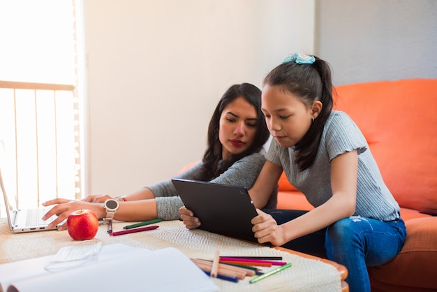 Joven madre soltera ayuda a su hija con los estudios en casa en la tableta
