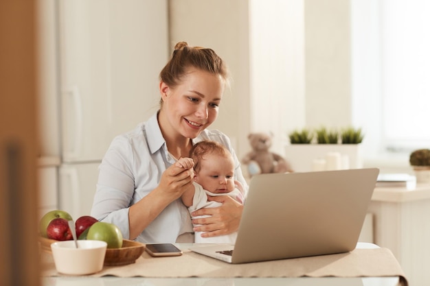 Joven madre sonriente mostrando dibujos animados en la computadora portátil al pequeño bebé