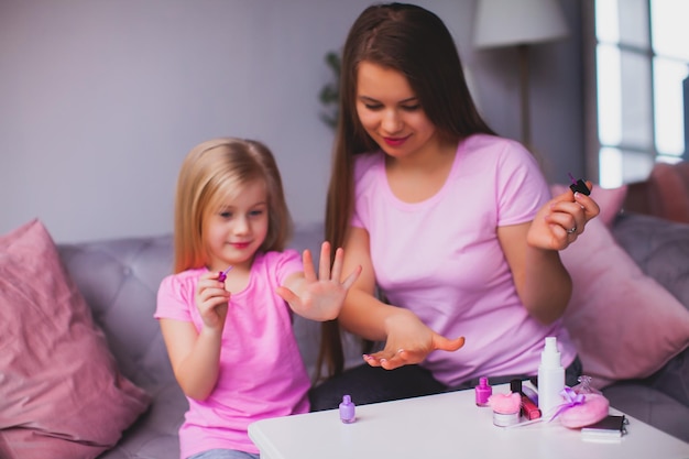 La joven madre sonriente y su hija muestran su manicura rosa La mujer y la niña visten ropa rosa y están sentadas en la habitación