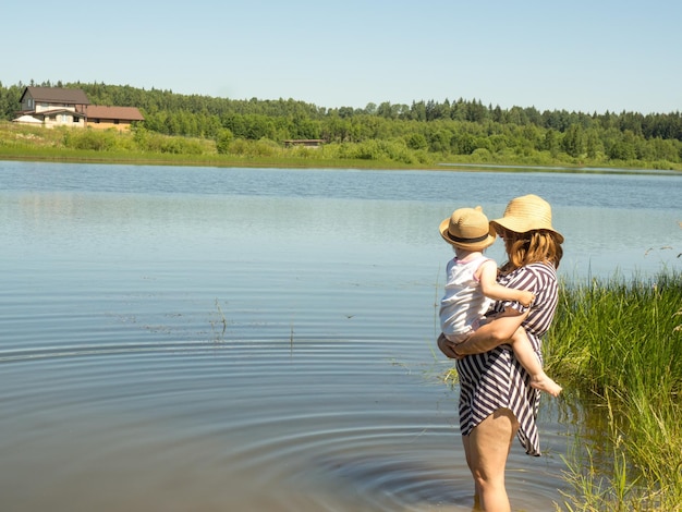 Una joven madre sostiene a su pequeña hija en brazos mientras nada en el lago Actividades de verano en la familia la madre le enseña al niño a regar