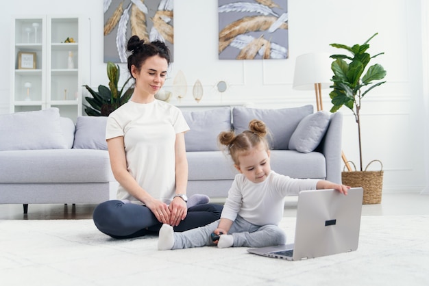 Joven madre y su adorable hija están usando la computadora portátil mientras está acostado en el piso.