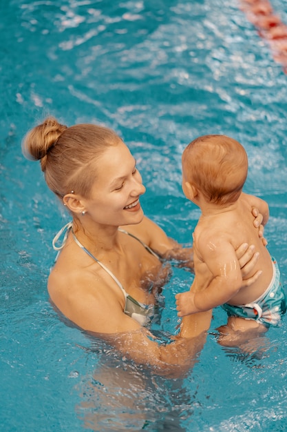 Joven madre y su bebé disfrutando de una lección de natación para bebés en la piscina. Niño divirtiéndose en el agua con mamá