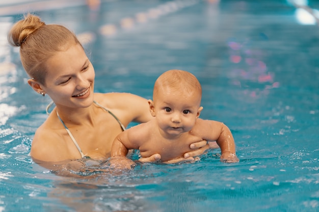 Joven madre y su bebé disfrutando de una lección de natación para bebés en la piscina. niño divirtiéndose en el agua con mamá