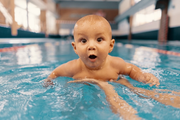 Joven madre y su bebé disfrutando de una lección de natación para bebés en la piscina. Niño divirtiéndose en el agua con mamá