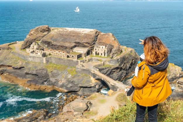 Una joven madre con su bebé mirando el Fort des Capucins, un islote rocoso en lo alto de un acantilado en la ciudad de Roscanvel, en la península de Crozon en Francia.