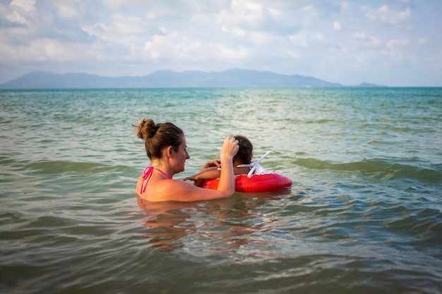 joven madre y su bebé Niño nadan en el mar. niño en un aro salvavidas inflable especial.
