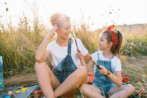 La joven madre y su hija se divierten. madre sonriente con hermosa hija dibuja la naturaleza