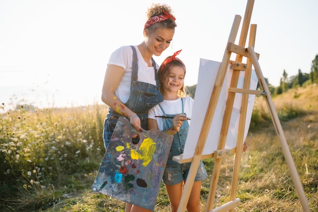 La joven madre y su hija se divierten. madre sonriente con hermosa hija dibuja la naturaleza