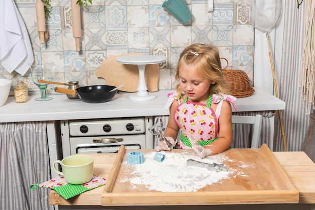 La joven madre y su hija están cocinando en la cocina con hermosos delantales