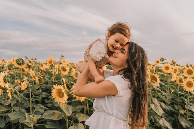 Joven madre con su hija en medio de un campo de girasoles al atardecer