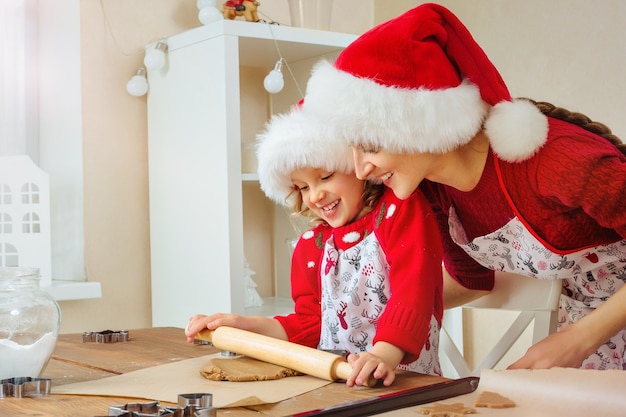 La joven madre y su hija recortan galletas de jengibre navideñas para felices fiestas con gorro de Papá Noel