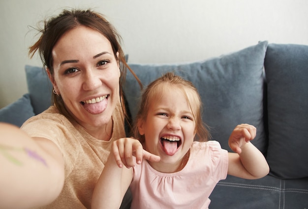 La joven madre con su hija se toman selfies y se divierten mirando a la cámara.