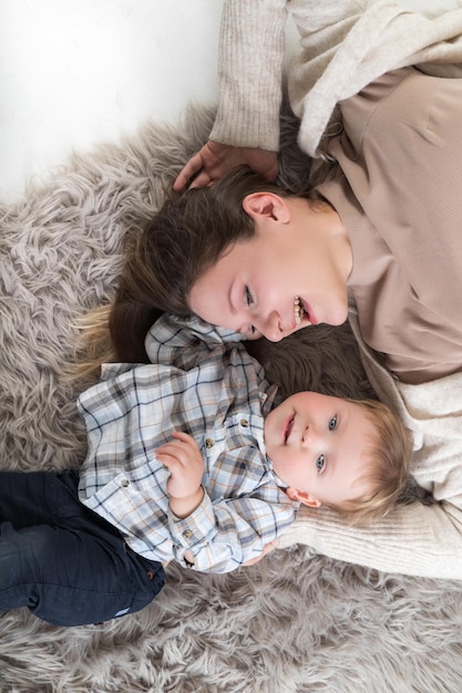 Una joven madre con su hijo se acuesta en una alfombra acogedora y se divierten juntos Vista superior