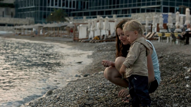 Una joven madre y su hijo arrojan piedras en el agua ondulante. Un niño creativo con mamá arroja piedras.