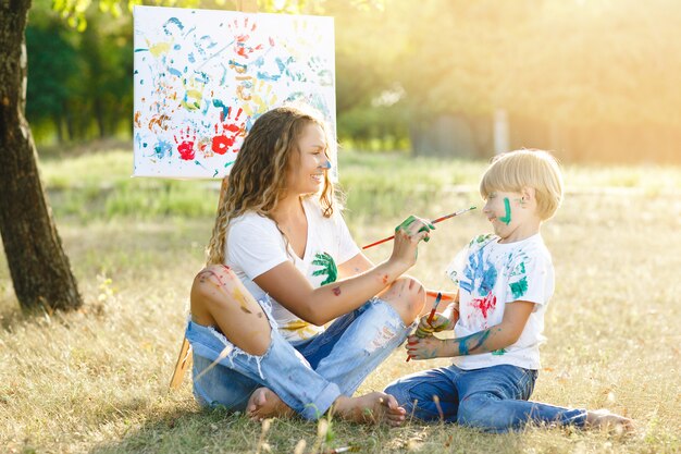 Joven madre y su hijo dibujando el uno al otro. Familia feliz al aire libre