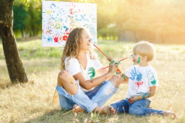 Joven madre y su hijo dibujando el uno al otro. Familia feliz al aire libre