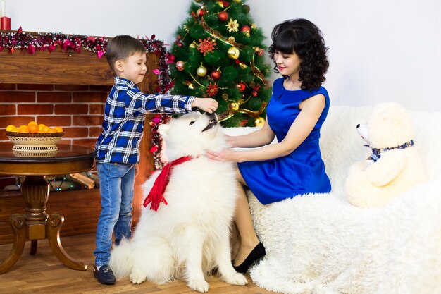 Una joven madre con su hijo y un perro en un árbol de Navidad.