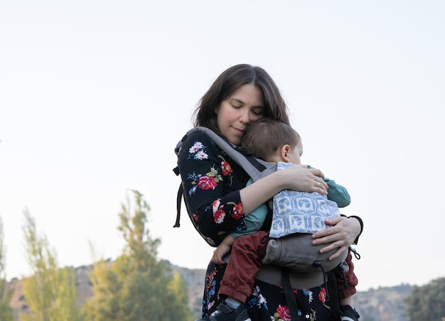 Joven madre con su niño pequeño en la espalda en un portabebés ergonómico en la naturaleza otoñal. Concepto de madre activa