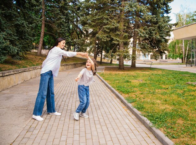 Una joven madre y su pequeña hija bailan en el parque. Una niña y una mujer están dando vueltas en la acera.