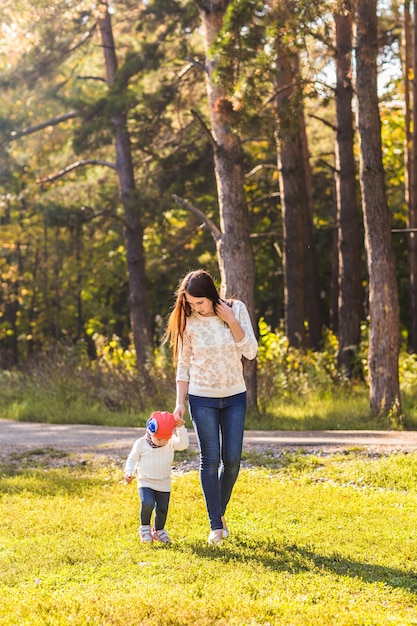 Joven madre con su pequeña niña en el parque de otoño.