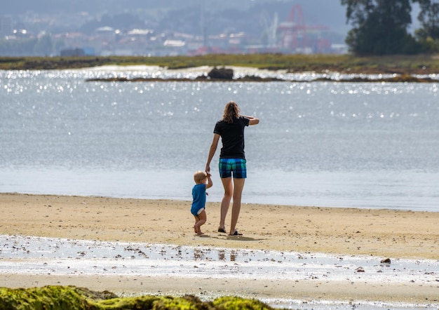 Joven madre y su pequeño hijo o bebé de un año caminando por la arena de la playa de Boiro Galicia