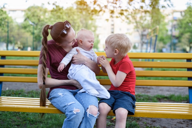 Joven madre y sus dos hijos en un banco en el parque