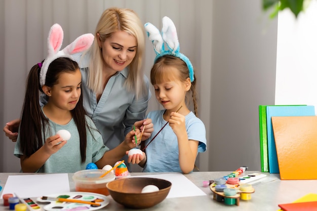 Joven madre y sus dos pequeñas hijas pintando coloridos huevos de Pascua en casa