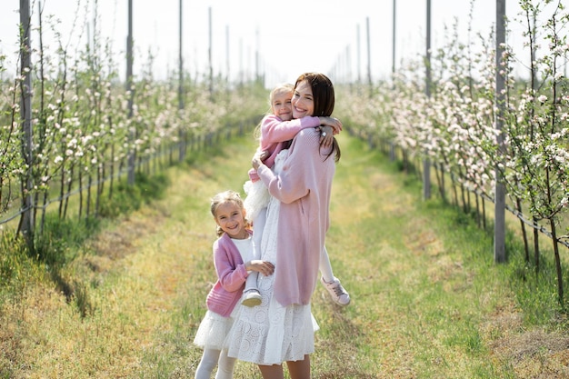 La joven madre y sus hijas gemelas caminan por un huerto de manzanas en primavera