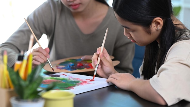 Joven maestra ayudando a una niña pintando un cuadro en la clase de arte