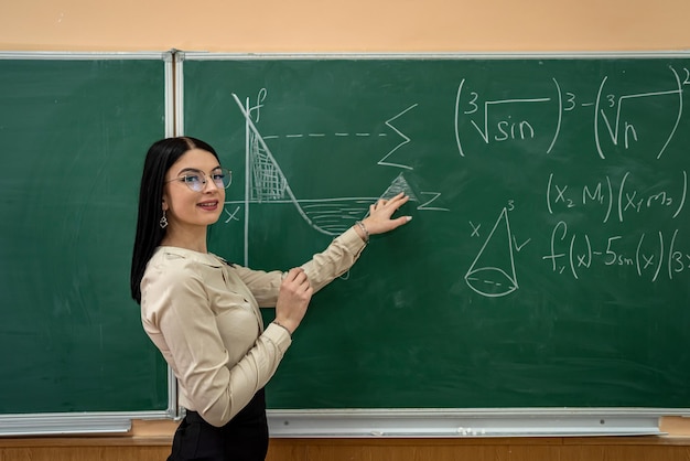 Joven maestra bonita escribiendo en una pizarra completando ecuaciones matemáticas en el aula