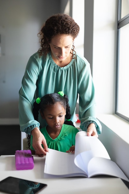 Foto joven maestra caucásica ayudando a una estudiante afroamericana que estudia en el escritorio en el aula