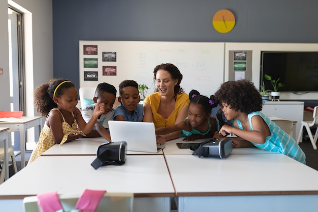 Joven maestra caucásica enseñando computadora portátil a estudiantes primarios afroamericanos en la clase
