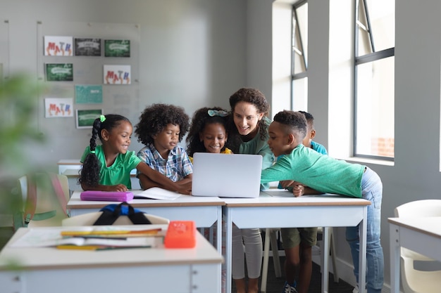 Joven maestra caucásica enseñando computadora portátil a estudiantes primarios afroamericanos