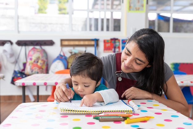 Joven maestra mexicana y niño en el aula de jardín de infantes, concepto de educación preescolar