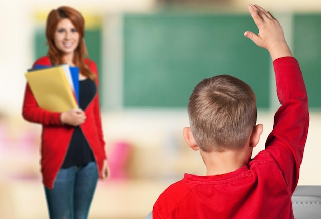 Joven maestra y niño con la mano levantada en la lección