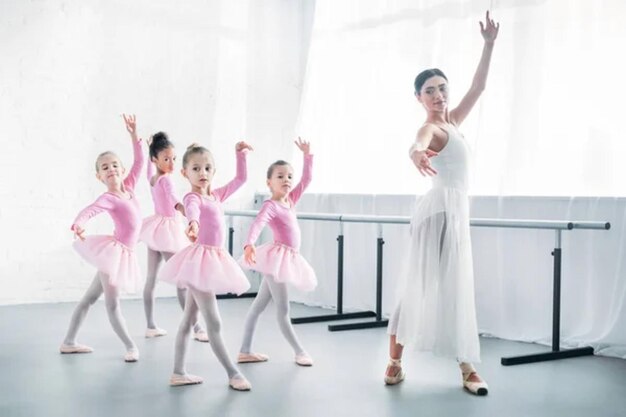 Joven maestra practicando ballet con niños adorables en faldas de tutu rosas