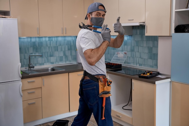 Joven maestro de casa en mascarilla mostrando el pulgar hacia arriba