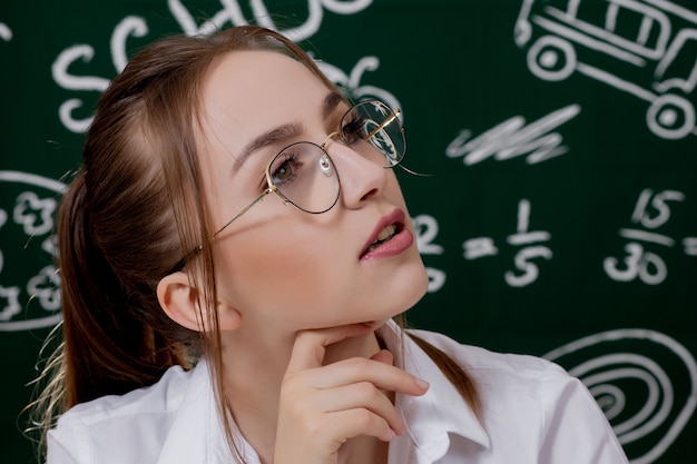 Joven maestro está sentado cerca de la pizarra en el aula