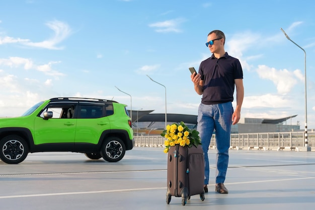 Joven con una maleta y flores en un estacionamiento del aeropuerto en un día soleado al atardecer Concepto de vacaciones