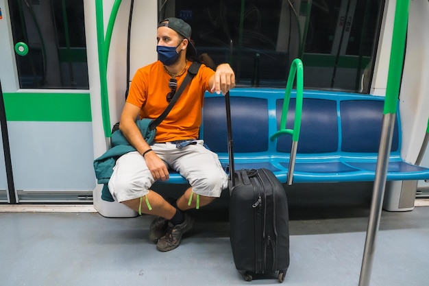 Un joven con maleta y sombrero sentado esperando el metro