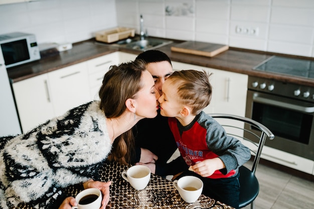 Joven mamá, papá y niño bebiendo café y té por la mañana. Concepto de familia, comida y personas.