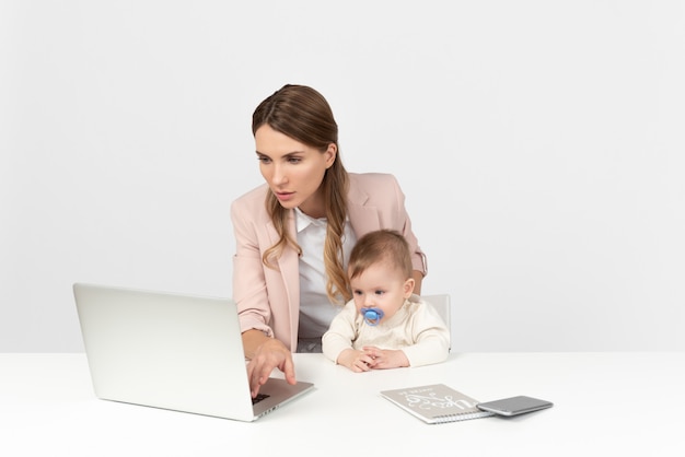 Joven mamá trabajando en computadora y cuidando niños