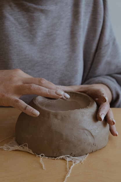 Una joven de manga larga gris hace un jarrón de arcilla con sus propias manos en un taller de escultura.