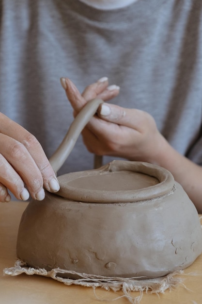 Una joven de manga larga gris hace un jarrón de arcilla con sus propias manos en un taller de escultura.