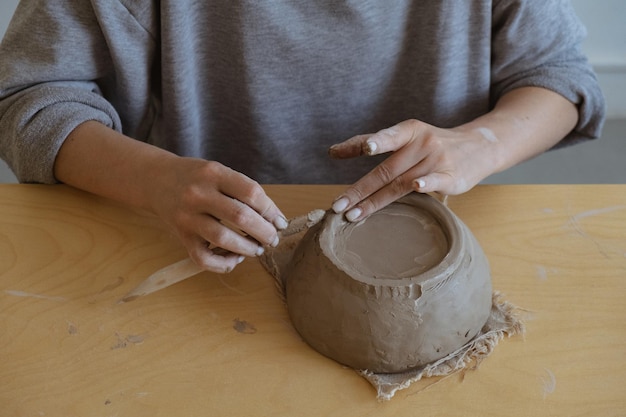 Una joven de manga larga gris hace un jarrón de arcilla con sus propias manos en un taller de escultura.